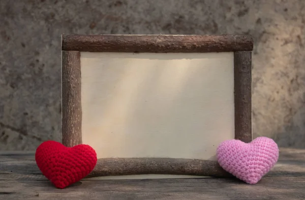 Marco de madera marrón en la mesa de madera áspera con los corazones de punto rojo y rosa en la esquina. Fondo de la pared de roca. La luz del sol brilla en el marco. Copiar espacio para editar y texto . — Foto de Stock