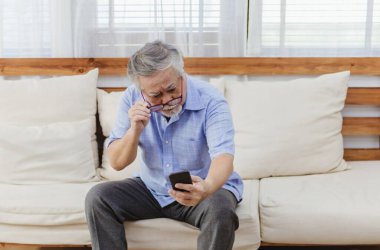 İnternette ya da sosyal medyada sörf yaptıktan sonra akıllı telefon kullanırken gözlük takan Asyalı kıdemli yorgun adam. Yaşlı, emekli erkek görme sorunu ya da yaşlılıktan kalma bulanık görme sorunu