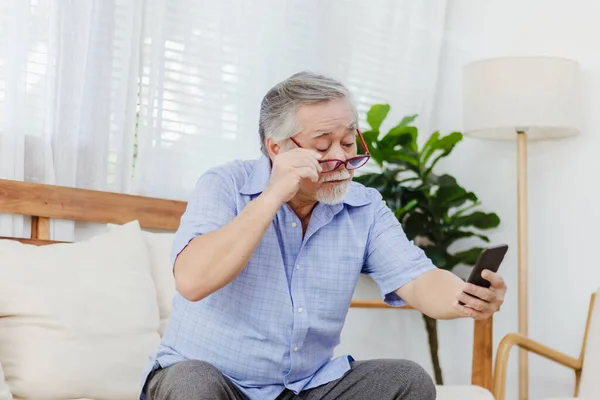 İnternette ya da sosyal medyada sörf yaptıktan sonra akıllı telefon kullanırken gözlük takan Asyalı kıdemli yorgun adam. Yaşlı, emekli erkek görme sorunu ya da yaşlılıktan kalma bulanık görme sorunu