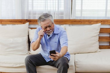 İnternette ya da sosyal medyada sörf yaptıktan sonra akıllı telefon kullanırken gözlük takan Asyalı kıdemli yorgun adam. Yaşlı, emekli erkek görme sorunu ya da yaşlılıktan kalma bulanık görme sorunu