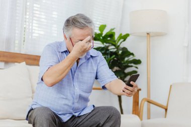 İnternette ya da sosyal medyada sörf yaptıktan sonra akıllı telefon kullanırken gözlük takan Asyalı kıdemli yorgun adam. Yaşlı, emekli erkek görme sorunu ya da yaşlılıktan kalma bulanık görme sorunu