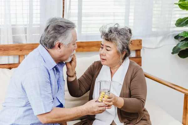 Asian couple woman caring sick elderly man by giving pill or drug at home. Love and relationship of retired senior couple. Health care and medicine of illness aged people photo concept.