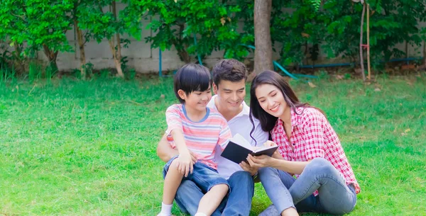 Mutlu aile babası, anne ve oğlu bahçede birlikte kitap okuyorlar. Ebeveynler ve çocuklar arasındaki mutluluk ilişkisi ya da bağ haftasonu eğlencesinin tadını çıkarın.