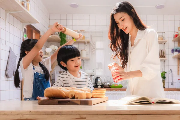 Happy and cute Asian family making food in kitchen at home together. Smiling mother, daughter and son enjoy making meal. Bonding of love between parent and children.