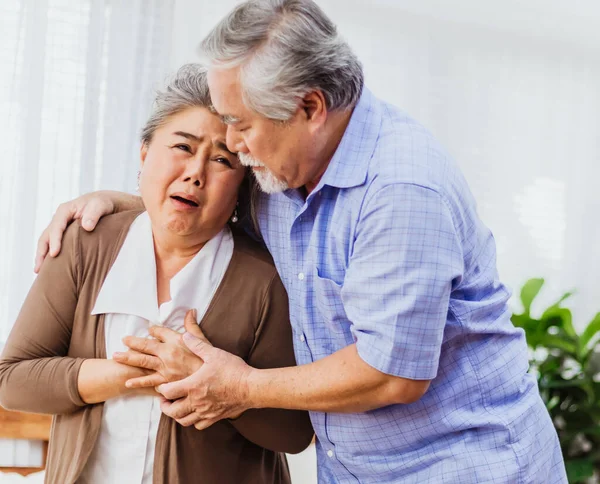 Retired Asian senior elderly wife pain from heart attack disease or illness with serious or worried husband take care at home. Medical emrgency treatment and health care insurance protection concept