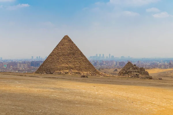 Camel karaván előtt a nagy piramis a Menkaure a Giza Piramis komplex háttérben Kairó város Skyline — Stock Fotó