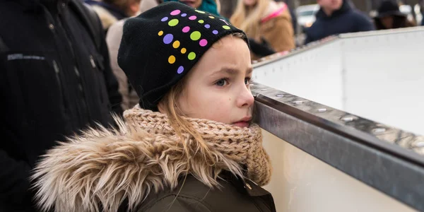 Smutná holčička sleduje lidi bruslit na ledě v parku — Stock fotografie