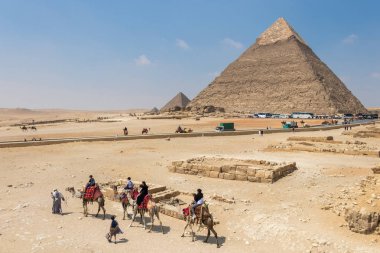 Turistler, Mısır 'daki Giza' da yaşayan bir adamın rehberliğinde Mısır 'daki piramitlerin önünde develere biniyor.