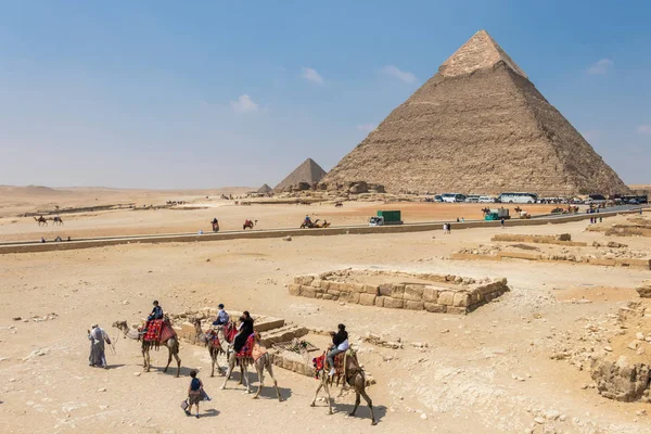 นักท่องเที่ยวขี่อูฐนําโดยชายท้องถิ่นที่กิซาต่อหน้าปิรามิด, อียิปต์ — ภาพถ่ายสต็อก