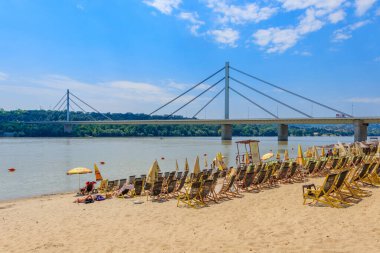 Novi Sad, Sırbistan - 3 Temmuz 2019: İnsanlar, Sırbistan 'ın Novi Sad kentindeki Liberty Köprüsü' nün (En Slobode) manzaralı Tuna Nehri üzerindeki plajın (Strand) tadını çıkarıyor