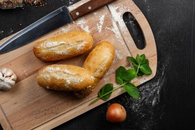 Kesme tahtasındaki taze beyaz ekmek üzerine siyah ahşap bir masaya un serpiştirilmiş baharatlar serpiştirilmiş.