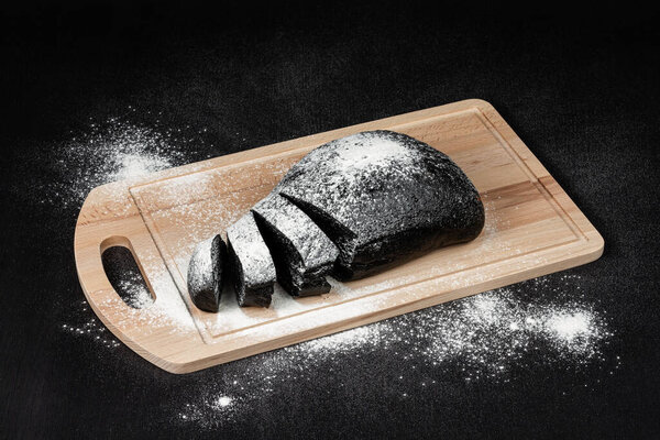 свежий черный ржаной хлеб на разделочной доске с мукой на черном деревянном столе
