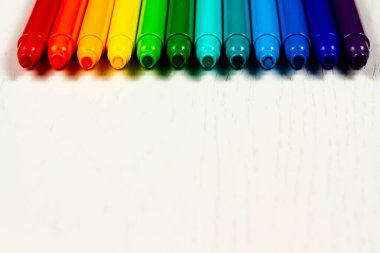 Parlak renkli keçeli kalemler beyaz ahşap bir masanın üzerinde duruyor.