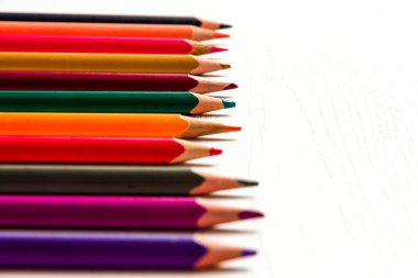 Birçok renkli sivri uçlu kalem beyaz ahşap bir masanın üzerinde yatar.