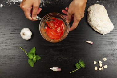 Aşçı kız taze İtalyan ev yapımı pizza yapmak için krema, sarımsak ve baharatla domates ezmesi karıştırıyor.