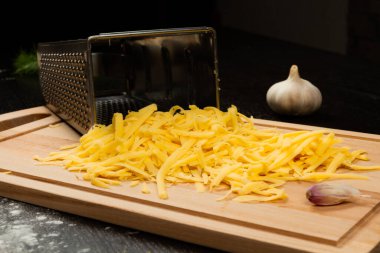 Pizza, sarımsak ve rende için rendelenmiş taze aromatik peynir ahşap mutfak tahtasının üzerinde yatıyor.