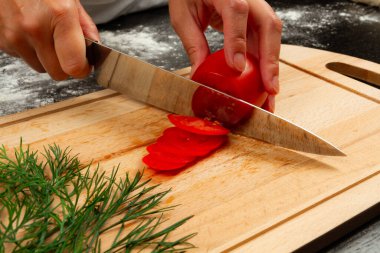 Kız şef, ahşap mutfak tahtasında İtalyan pizzası yapmak için taze kokulu domates keser.