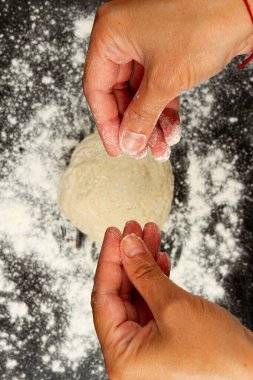 Şef kız, ev yapımı hamur yapmak için siyah ahşap mutfak masasına un serpiyor.