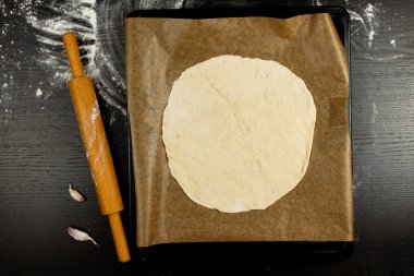 Maya hamurundan yapılmış pizza tepsisi siyah ahşap bir masada parşömen kağıdının üzerinde yatıyor.