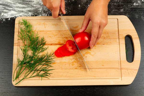 girl chef cuts fresh fragrant tomatoes for making italian pizza on wooden kitchen board