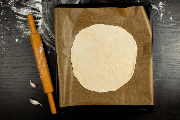 Maya hamurundan yapılmış pizza tepsisi siyah ahşap bir masada parşömen kağıdının üzerinde yatıyor.