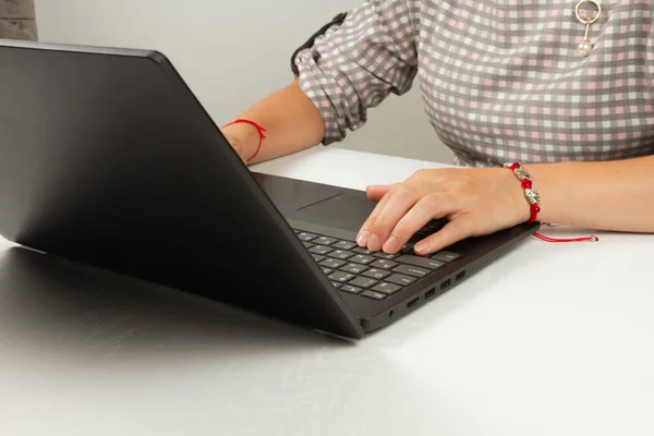 female hands are typing text on laptop keyboard on white wooden table background
