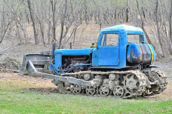 An old caterpillar tractor with an excavator scraper stands on the road