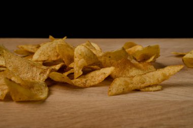 İştah açıcı patates cipsleri ahşap bir tahtaya saçılmış.
