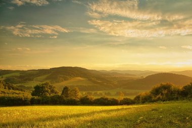 Tepelik manzara üzerinde gün batımı, batan güneşin altın parıltısı, ön planda çayır