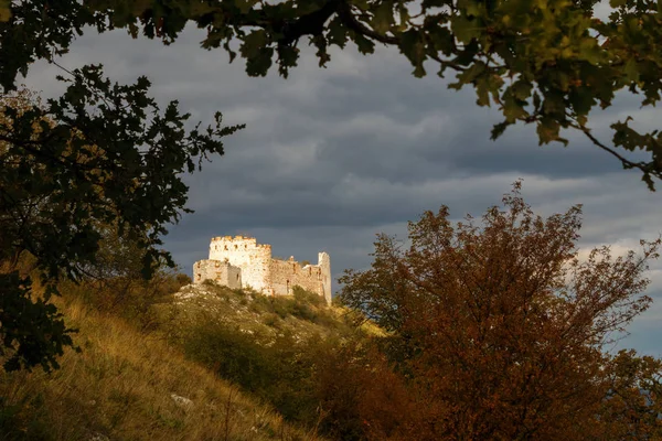 Castle in autumn - Huge ruins of Devicky Castle on Palava hills, Czech republic, dark cloudy sky, ruins lit by autumn sun