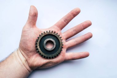 Adamın eli paslı bir vites tekerleğini beyaz bir arka planda tutuyor.