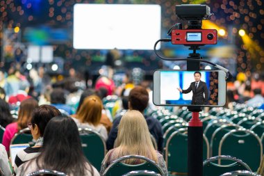 Closeup akıllı cep telefonu Live Asya işadamı seyirci konferans salonunda, fotoğrafçı ya da Video ve Live Streaming kavramı için kamera üzerinden tage hakkında bilgi veren alarak
