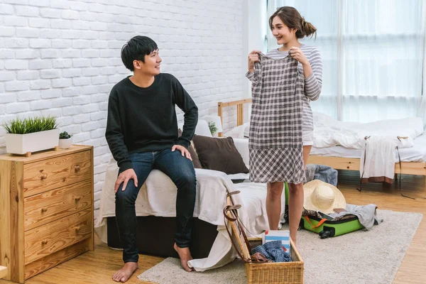 Happy Asian Couple choosing the clothes for preparing to travel in living room at the modern home, Couple, life style and traveler concept,