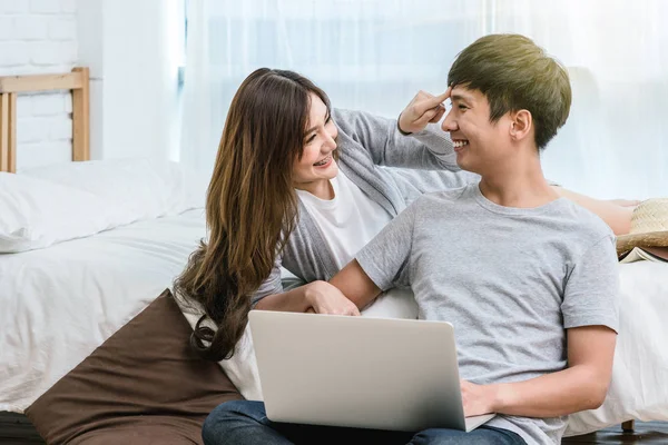 Closeup Happy Asian Lover or couple talking and smiling when using technology laptop on the bed in bed room at modern home, young women pointing to the forehead of boyfriend, Lover and life style concept,