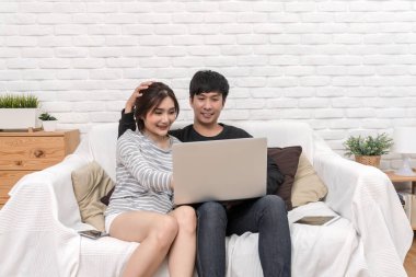 Mutlu Asya sevgilisi oturma ve dijital dizüstü modern ev, yaşam tarzı ve sevgili meslektaşım kavramı, oturma odası kanepe üzerinde neşeli eylem kullanma