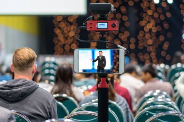 Closeup akıllı cep telefonu Live Asya işadamı seyirci konferans salonunda, fotoğrafçı ya da Video ve Live Streaming kavramı için kamera üzerinden tage hakkında bilgi veren alarak