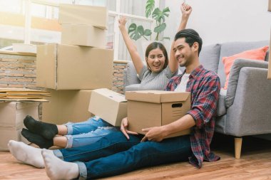 Asian young couple are glad after successfull packing the big cardboard box for moving in new house, Moving and House Hunting concept, clipart