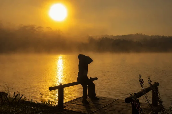 孤独の概念と劇的な日の出時に屋形船川湖に手アクションで頭に坐っているシルエット落ち込んで人 — ストック写真