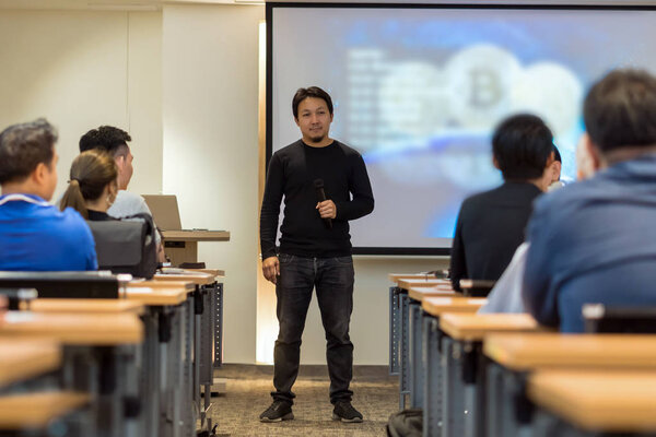 Asian Speaker with casual suit on the stage in low light over the presentation screen in the business or education seminar