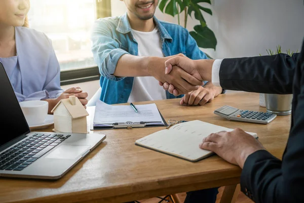 Sale representative offer the house key chain to Asian young couple after signed contact house purchase or rental on the working space table in new house,Moving and House Hunting concept