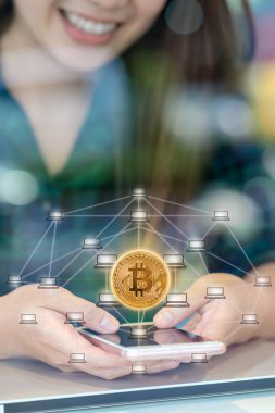 Bitcoins mockup ve dağıtılmış bilgisayar ağ hologram alanı, blockchain ve bitcoin kavramı ortak çalışma İşyerinde akıllı cep telefonu kullanarak Closeup Asya iş kadını ele