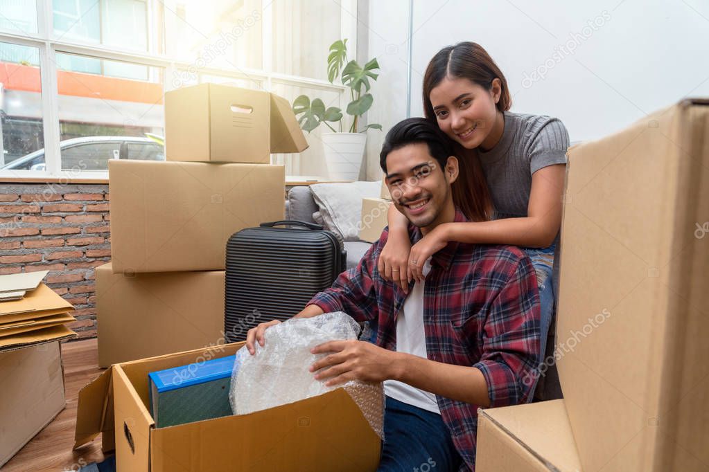 Asian young couple packing into big cardboard box for moving in new house, Sitting on difference step between sofa and floor and hug at the relax time, Moving and House Hunting concept
