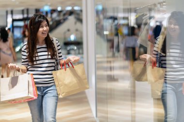 Alışveriş çantası tutarak ve cam mağaza üzerinden yeni moda elbiseler arıyorum mutlu Asyalı kadın