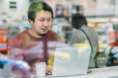 Modern ofis, iş ve yaşam tarzı konsept cam yanındaki masada mutluluk başında çalışmak için teknoloji dizüstü kullanarak rahat kıyafetli Asyalı işadamı portresi