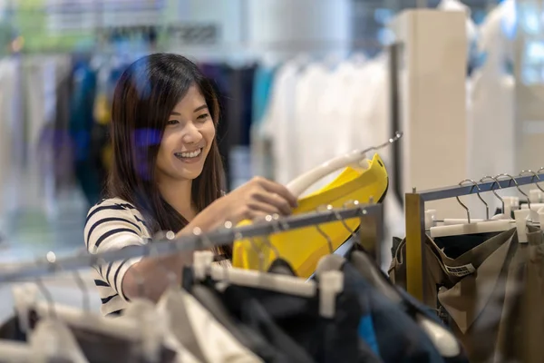 愉快的亚洲妇女选择衣服和裙子在玻璃商店商店与愉快的行动在部门中心 — 图库照片