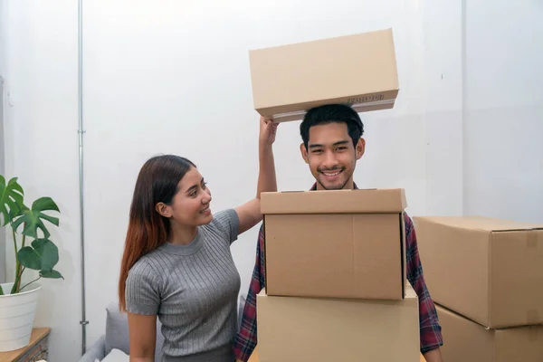 Asian young couple carrying big cardboard box for moving in new house, Helping relocate and joshing together, Moving and House Hunting concept