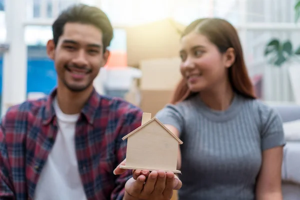 Closeup Asian young couple holding the house model in Love and glad feeling after successfull packing the big cardboard box for moving in new house, Moving and House Hunting concept,