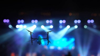 Konser kalabalığının videosu için uçan Drone 'un yakın çekim silueti ve konferans salonundaki spot ışıklarının bulanık fotoğrafı, müzikal ve konser konsepti