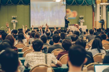 Konferans salonu veya Seminer Toplantı, iş ve eğitim kavramı sahne alanı'ndaki hoparlörden soruyu cevaplamak için el gösterilen seyirci arkadan görünüş