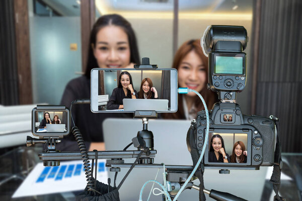 Набор камер со смартфоном и экшн-камерой на штативе над двумя азиатскими молодыми предпринимательницами, дающими интервью в прямом эфире, Live Streaming for the enterprise concept
